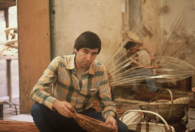 young Allan H Palecek weaving a basket in a plaid shirt